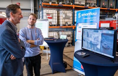 Twee mannen in een magazijn kijken naar een scherm met informatie over smarttechnologie. Achtergrond met opslagrekken.