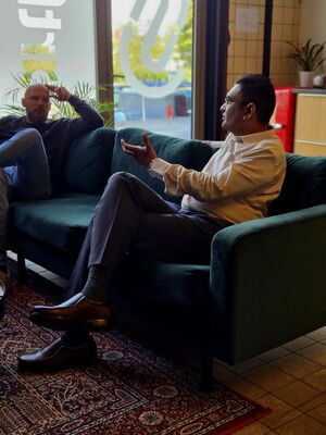 Twee mannen zitten op een groene bank en voeren een gesprek in een moderne omgeving.