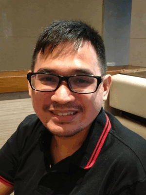 Een enthousiaste man met een bril en zwart t-shirt, zittend in een restaurant.