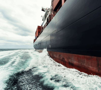 Zijaanzicht van een container schip met golven eromheen onder een bewolkte lucht.