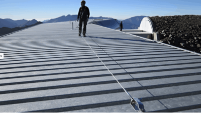 Een persoon staat op een plat dak met een veiligheidslijn, met een bergachtig landschap op de achtergrond.