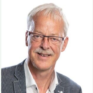 Een professioneel portret van een man met grijs haar, een bril en een blazer, glimlachend naar de camera.