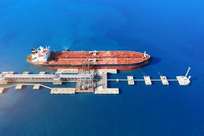 Een tanker ligt aangemeerd bij een haven, met een heldere blauwe zee op de achtergrond.