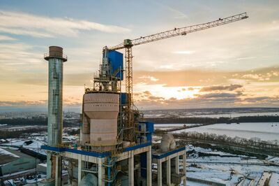 Bouwplaats met een kraan en een grote constructie bij zonsondergang, omgeven door sneeuwlandschap.