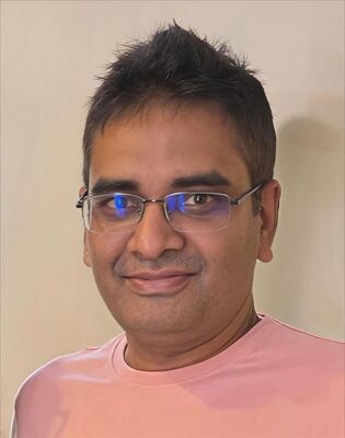 Een man met een kort kapsel en bril, kijkend naar de camera, met een neutrale achtergrond.