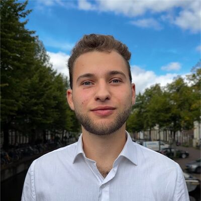 Jonge man met een lichte huid en een baard, gekleed in een wit overhemd, staand in een groene omgeving met blauwe lucht.