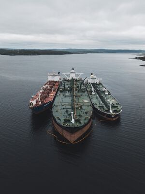 Drie schepen liggen naast elkaar in een rustige haven, omringd door water en een bewolkte lucht.