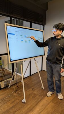 Man wijst naar een scherm met informatie in een vergaderruimte.